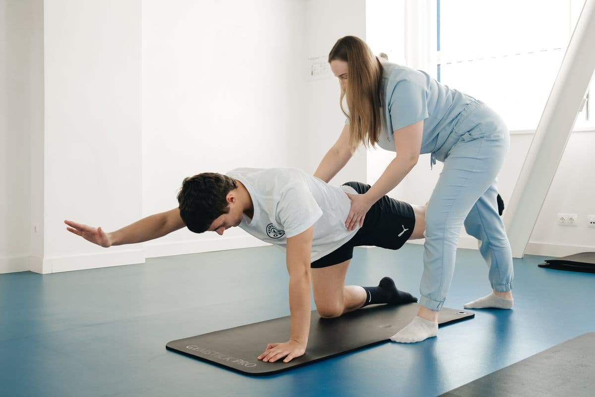 Physiotherapist supporting a patient doing a core stability exercise on a mat