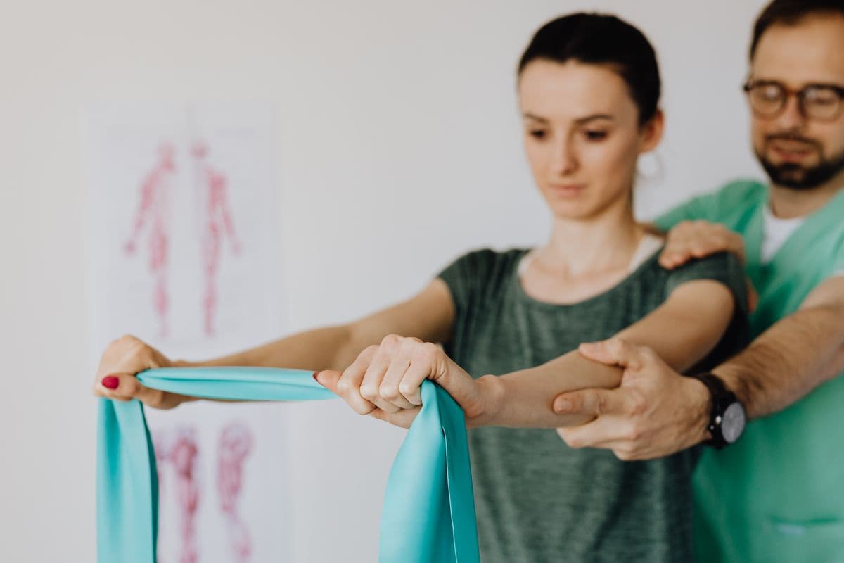 Patient pulling a resistance band while the physiotherapist supports her shoulder