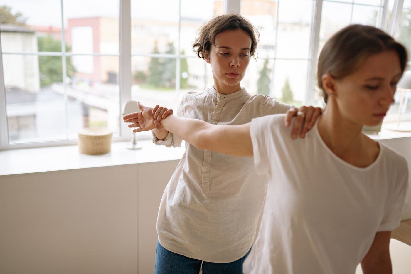 Therapist helping a patient stretch her arm in a bright room at home